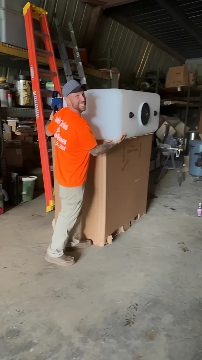 A man in an orange shirt moving a large appliance in a warehouse.