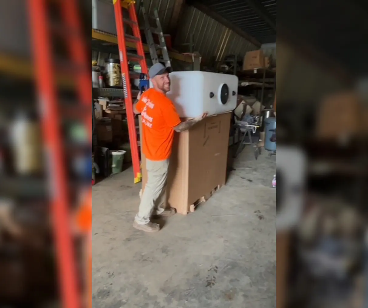Man in orange shirt working with a large cardboard box in a warehouse.
