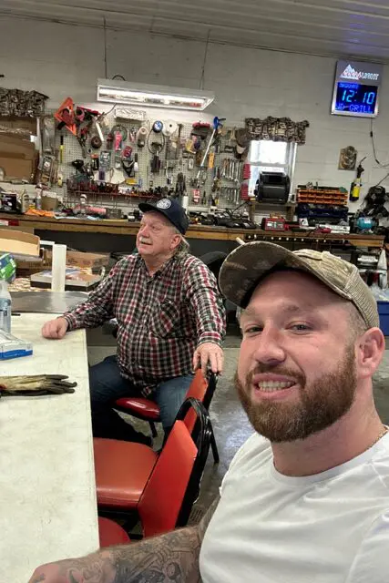 Two men smiling at a counter in a rustic store.