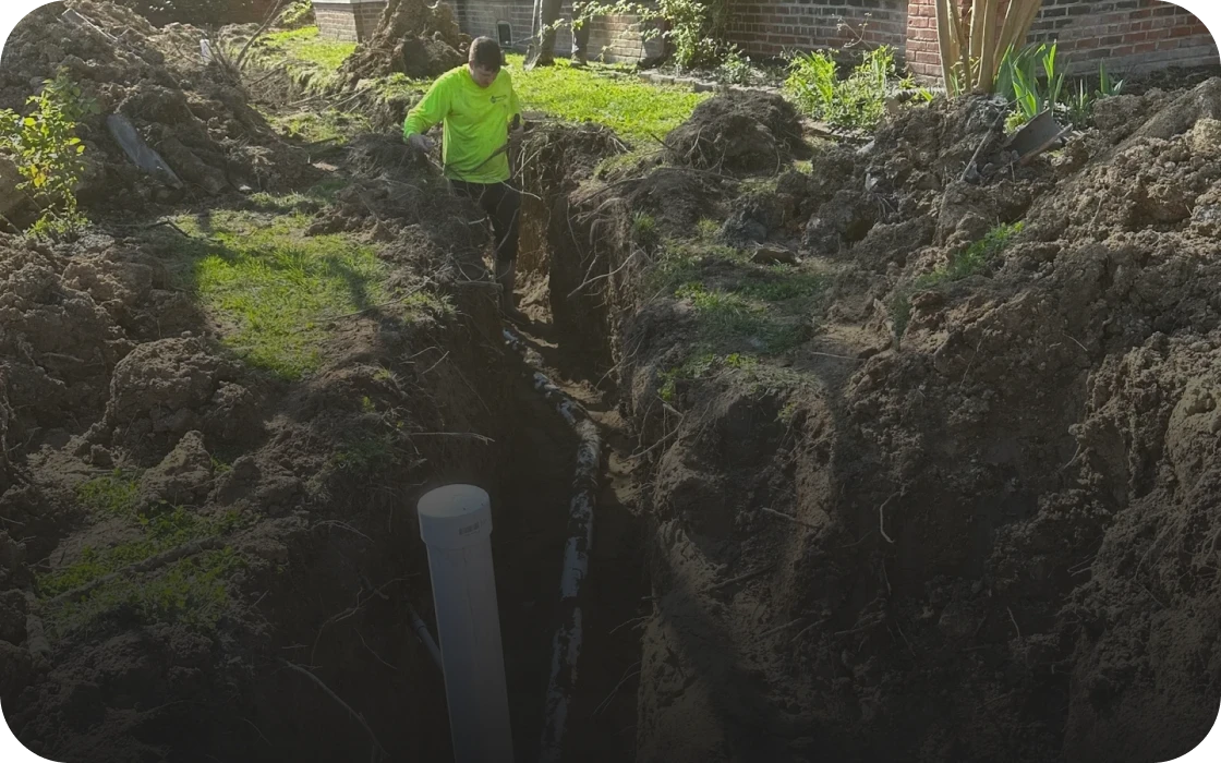Person inspecting trench with pipe installation.