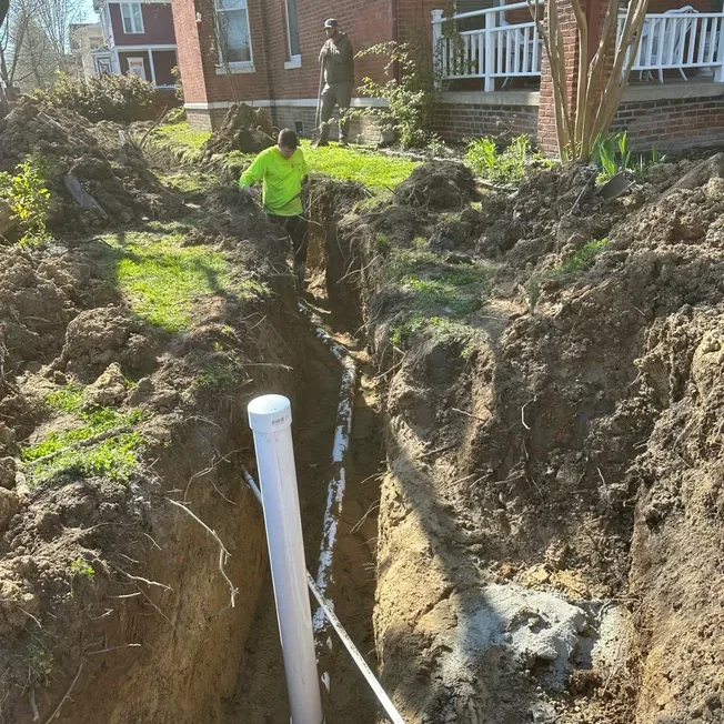 Workers digging trench next to brick house.