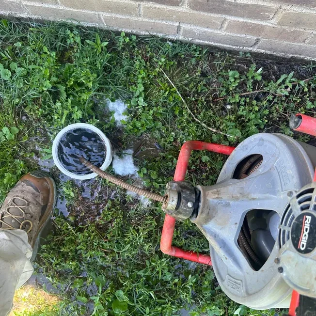 Drain cleaning machine in use near wall.